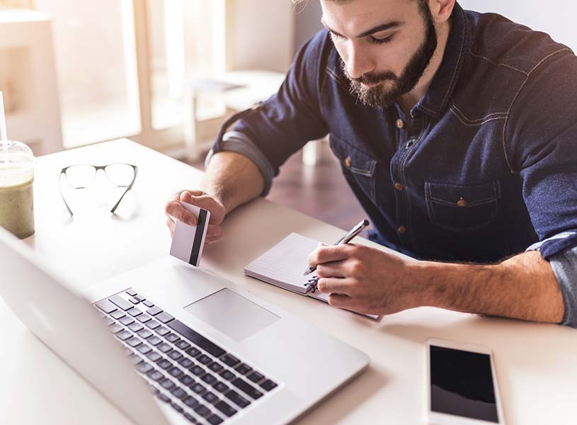 A young man using a credit or debit card at a laptop computer